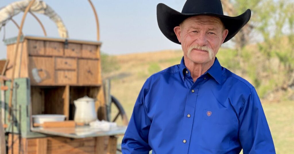 A man in a cowboy hat stands proudly in front of a wagon, embodying the spirit of BBQ cooking challenges.