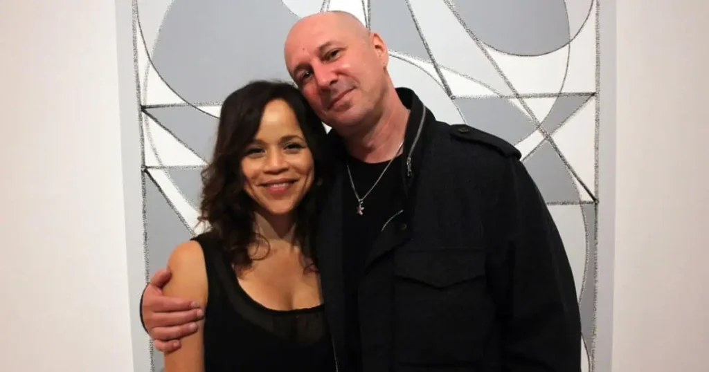 A man and woman stand beside each other, posing in front of a painting related to Eric Haze's personal life.