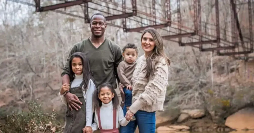 A family stands together for a photo in front of a bridge, capturing a moment related to Raheem Morris's Personal Information.