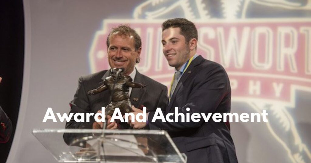  Two men proudly hold an award, with one smiling, celebrating their achievements together in a moment of success.